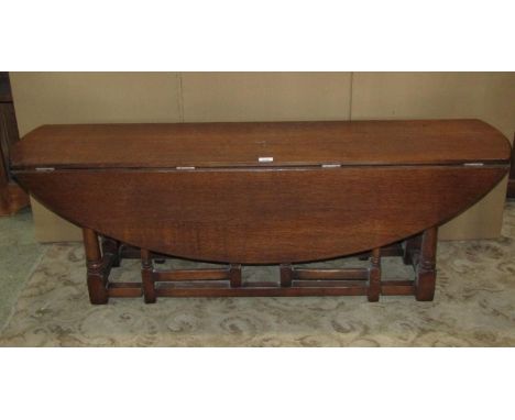 A low oak oval drop leaf gate leg 'Wakes' table in the old English style raised on turned gun barrel supports united by stret