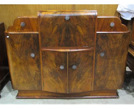 An Art Deco style walnut veneered cocktail cabinet, the central fall front enclosing a rising shelf and mirror lined interior