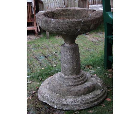 A large weathered natural stone bird bath/planter, the circular shallow bowl with notched channel raised on a cylindrical pil