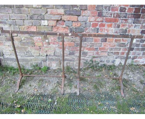 A pair of old iron work trestles with simple swept supports, supporting an associated stripped pine boarded top with cleated 