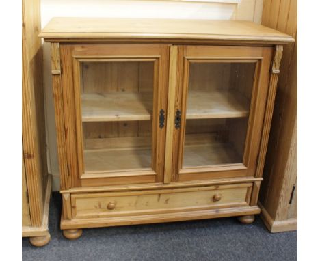 A pine cupboard with two glazed panel doors enclosing shelf, with frieze drawer below, on turned legs 97cm
