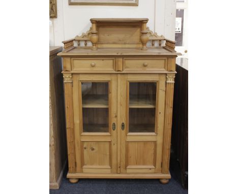 A pine cabinet the three quarter gallery top with central raised shelf, above two drawers and two glazed panel doors enclosin