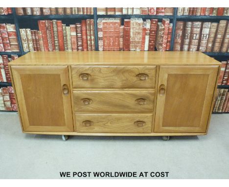 An Ercol light elm sideboard with three drawers flanked by two cupboards (H70 x W156 x D44cm)