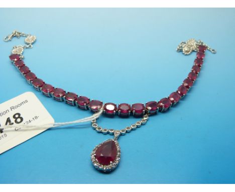A silver necklace set with 23 oval cut rubies and a drop section set with a large pear cut ruby surrounded by white sapphires