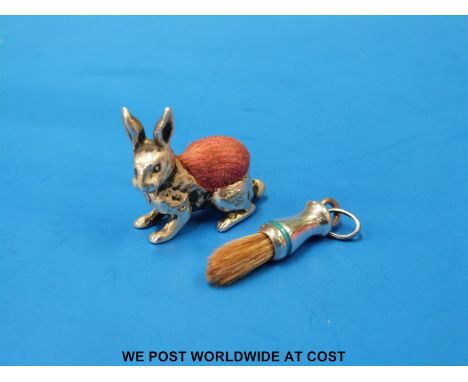 A hallmarked silver hare pin cushion, (length 3cm) together with a white metal and enamel miniature brush marked 925