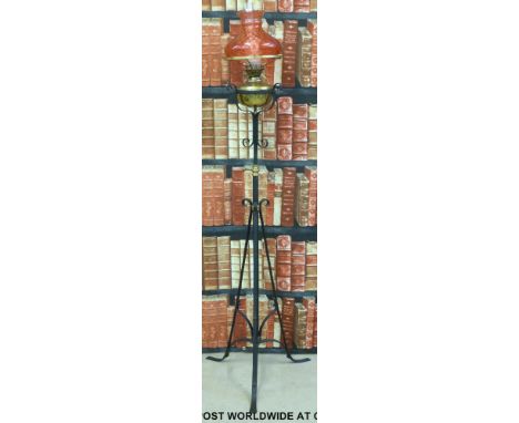 A 19thC wrought iron extending oil lamp converted to electricity with cranberry glass shade height 161cm