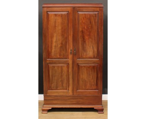 A George III Revival mahogany wardrobe, moulded cornice above a pair of doors set with raised and fielded panels, bracket fee