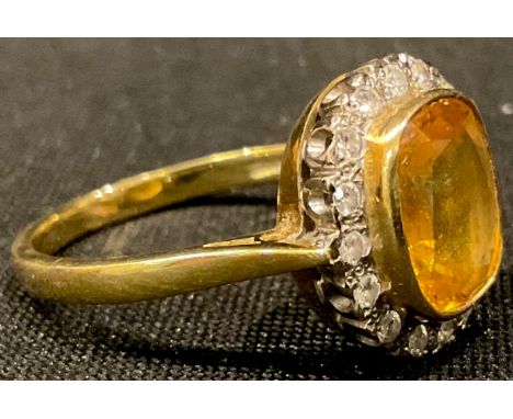 An 18ct gold yellow sapphire and diamond ring, the central cusion cut stone surrounded by sixteen illusion set diamond chips,