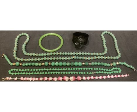 A carved moulded black plastic jet type cuff bracelet; a jadeite bangle; a string of jadeite beads; a string of glass beads; 