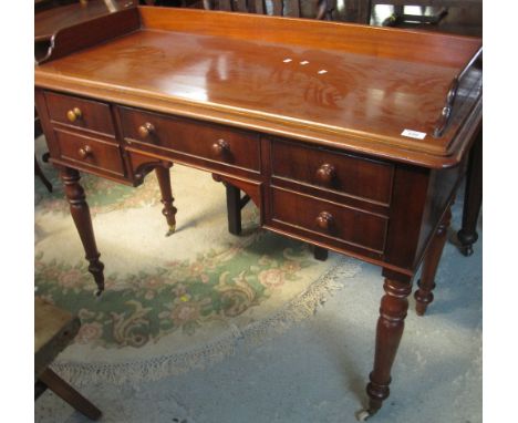 Victorian mahogany kneehole desk with gallery top and an arrangement of drawers, on baluster turned legs and ceramic casters.