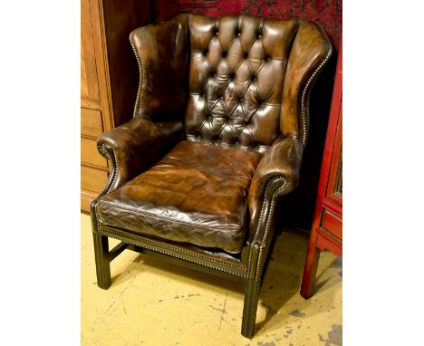 WING ARMCHAIR, George III style ebonised in buttoned brown leather with cushion seat, 83cm W. 