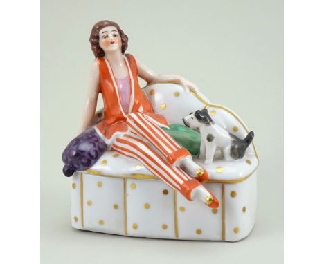 Glazed china seated Deco Lady dressing table box, 1920s, lady in orange and white outfit, reclining on a white and gold spott