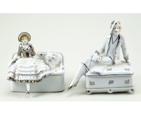 Two glazed china dressing table boxes, 1920s, both finished in white with silver decoration, seated lady with dog on couch sh