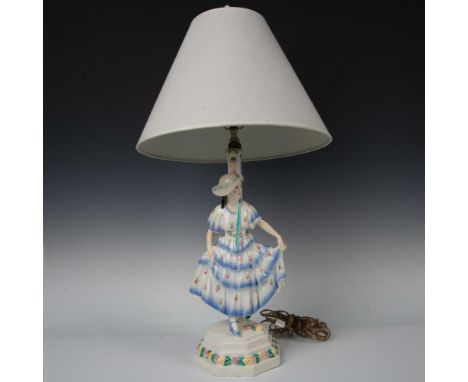 A glazed painted table lamp featuring a lady in a blue and white ruffled dress with pink flowers. Pink and yellow modelled fl