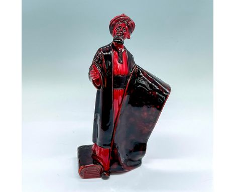 Glazed figure of a man in a turban holding a carpet for sale. Red with black accents. Royal Doulton Flambe backstamp. Artist: