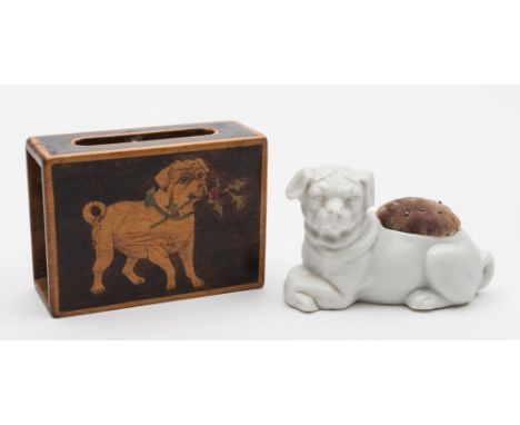 A bisque porcelain pug pin cushion and a matchbox cover: the former modelled recumbent with crossed fore paws, in the white, 