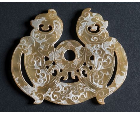 A Chinese calcified jade amulet: in archaic Han Dynasty style, carved and reticulated with two dragons around a central ring,