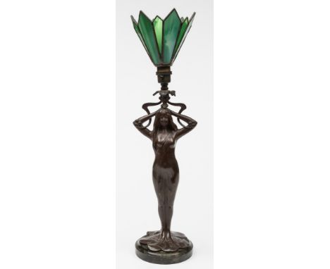 An Art Nouveau influence bronzed metal table lamp: the semi naked female partially draped and supporting a foliate decorated 