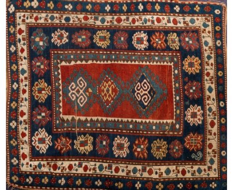 A Kazak rug:, the red oblong central panel with triple hooked geometric medallions, enclosed by indigo and ivory triple borde