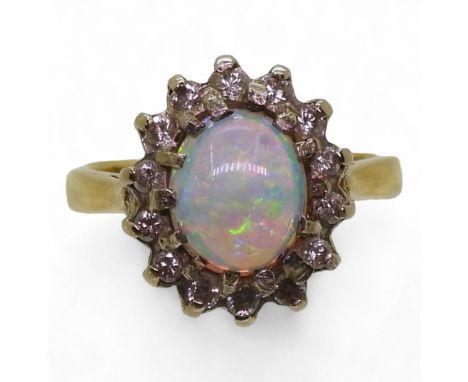 An 18ct gold opal and diamond ring, set with a white opal with good colour play of approx 8.5mm x 6.5mm x 3.8mm, surrounded w