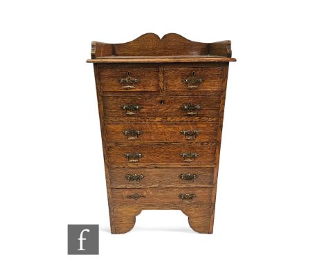 A small Edwardian light oak office style chest of two short and five long drawers, brass aesthetic drop handles below a tray 