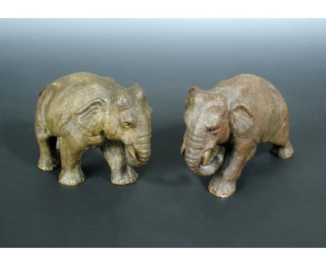 A pair of early 20th century bronze elephants, both depicted walking, the male elephant with a leaf suspended from a crescent