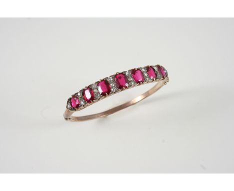 AN EARLY 20TH CENTURY DIAMOND AND SYNTHETIC RUBY HALF HINGED BANGLE millegrain set with circular-cut diamonds and seven oval-