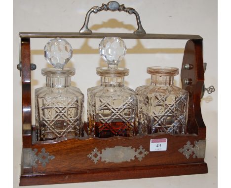 An early 20th century oak three bottle tantalus having silver plated mounts and locking stile with key (one decanter lacking 