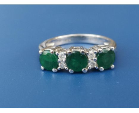 A modern three stone emerald ring with four small diamonds in 18ct white giold.  Finger size K/L.