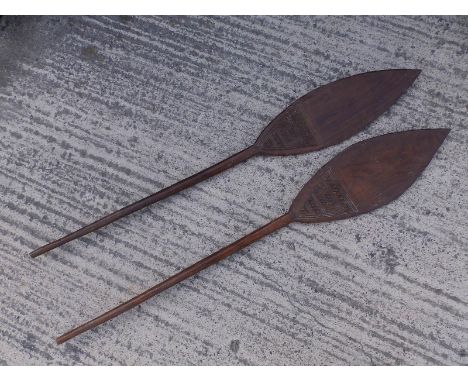 A pair of African carved wood paddles, each having a triangular panel of geometric decoration to one side, 53.5" &amp; 54" ov