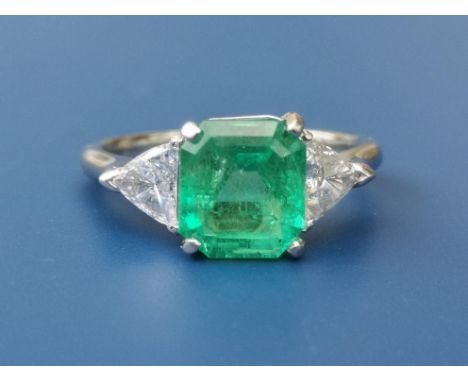 A three stone 2.57 carat emerald &amp; diamond set platinum ring, the rectangular cut four-claw set emerald flanked by two tr