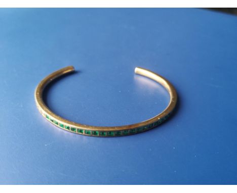 An emerald set 18ct gold bangle, of open-ended hoop form, maximum internal dimension approximately 55mm.