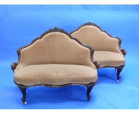 A pair of Victorian carved walnut crinoline Sofas, each with a shaped back carved with scrolls, serpentine apron and cabriole