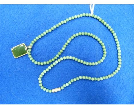 A jade circular bead Necklace, the yellow metal bound clasp with green hard-stone pendant, suspended, in a yellow metal mount