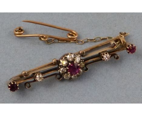 A ruby and diamond bar brooch, comprising a cluster with central ruby surrounded by diamonds on an open scrolling framework m