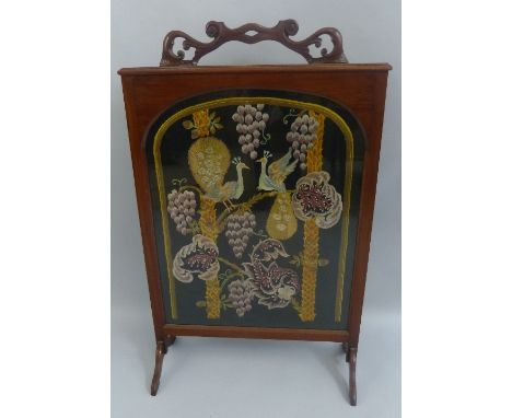 An early 20th Century mahogany fire screen, with pierced scrolling crest/handle over an oblong framed glazed arched silk thre
