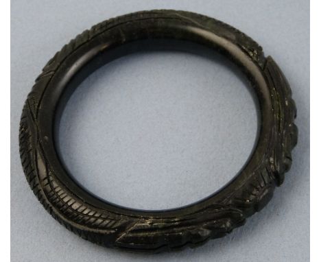 A Chinese black jade bangle, carved with two dragons chasing a flaming pearl, 8.5cm diameter 