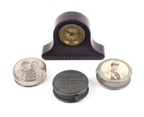 Four tape measures comprising a novelty composition example as a mantel clock, 7.5cm, a circular tin example for Cox and Co, 