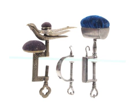 Three metal sewing clamps comprising a brass hemming bird example, the rectangular frame with pin cushion, the spring bird wi