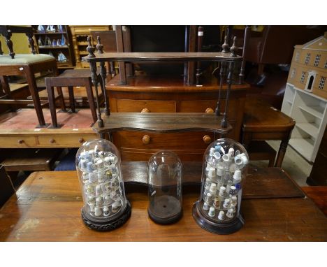 A small collection of ceramic and brass souvenir thimbles with three glass domes on hardwood stands (two with display shelves