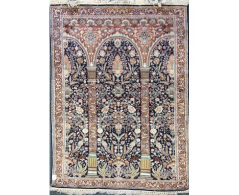 AN EASTERN SILK CARPET worked with an architectural design of arched top columns for a floral and foliate pattern against a d