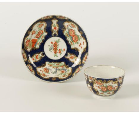 A WORCESTER PORCELAIN TEA CUP AND SAUCER with polychrome painted kakiemon decoration within gilt cartouches, on scale blue gr