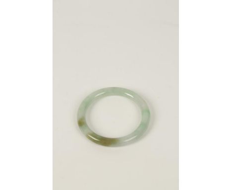 A CHINESE JADE BANGLE of plain circular form, of celadon colour with dark to light green inclusions throughout, 9cm dia.