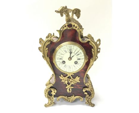 A French ornately decorated mantel clock with simulated tortoiseshell case, presenting a brass mythical creature to the top. 