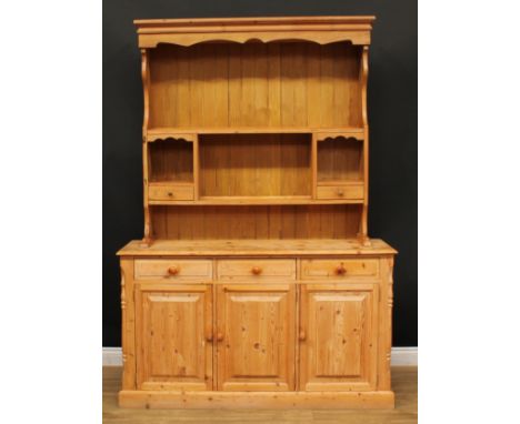 A farmhouse pine dresser, shaped apron above two plate racks, a pair of open niches and two small drawers, the projecting bas