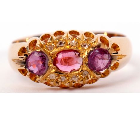 Early 20th century 18ct gold, ruby and diamond ring centring an oval shaped ruby between two circular cut rubies and highligh