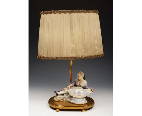 A PORCELAIN TABLE LAMP in the form of a reclining female figure on an oval brass base with shade, 46cm high overall