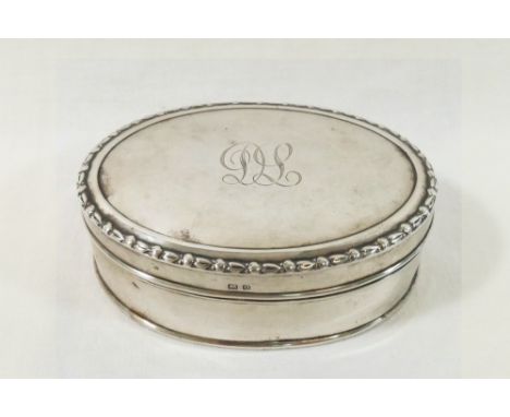 A silver oval hinged dressing table trinket box, with hinged lid engraved with scrolling initials, and blue satin lined inter