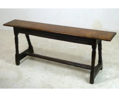 A 17th century and later oak bench, with chip caved decoration the frieze, raised on turned legs joined by a trestle stretche