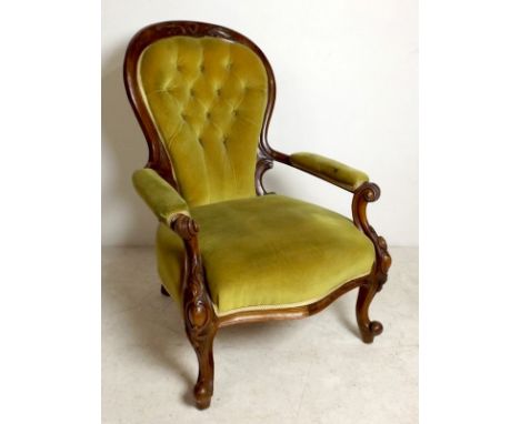 A Victorian walnut armchair, with green velvet upholstered button back, the frame carved with scrollwork, the scroll knop leg